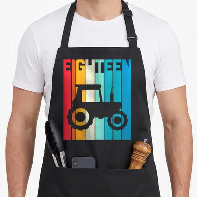 Tablier de cuisine noir avec motif rétro tracteur agricole et texte EIGHTEEN sur bandes colorées verticales.