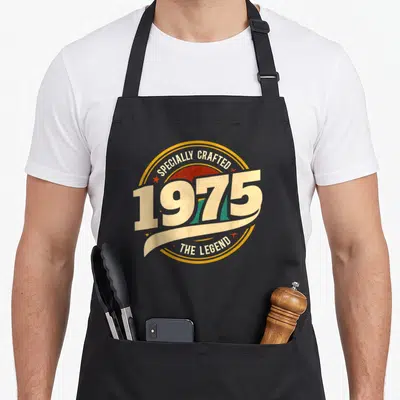Tablier de cuisine noir avec logo vintage 1975 Specially Crafted The Legend en jaune et rouge.