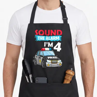 Tablier de cuisine noir avec une voiture de police dessinée et le texte Sound The Alarm I'M 4 en lettres colorées.
