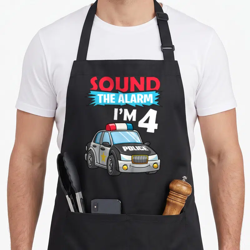 Tablier de cuisine noir avec une voiture de police dessinée et le texte Sound The Alarm I'M 4 en lettres colorées.