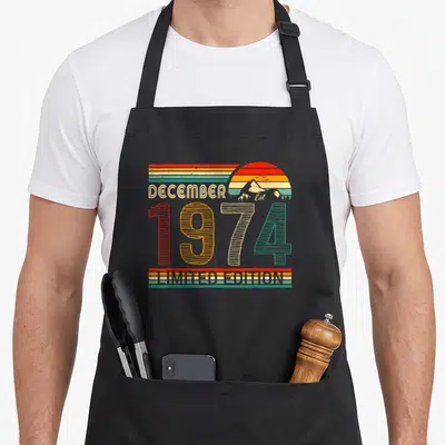 Tablier de cuisine noir avec l'inscription Décembre 1974 Limited Edition et un soleil retro coloré.