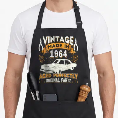 Tablier de cuisine noir avec illustration voiture vintage et texte Aged Perfectly Original Parts en orange et blanc.