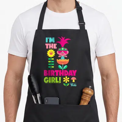 Tablier de cuisine noir avec Poppy et le texte I'm the anniversaire Girl entouré de fleurs colorées.