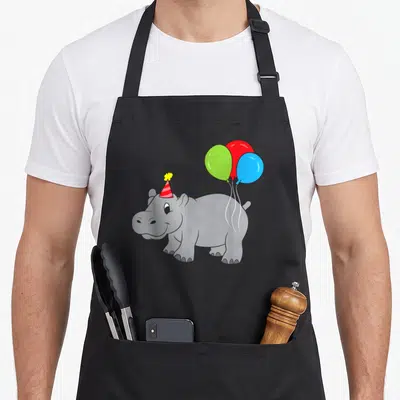 Tablier de cuisine noir avec illustration d'un hippopotame portant un chapeau de fête et des ballons verts rouges et bleus.