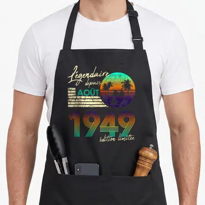 Tablier de cuisine noir avec design rétro coloré affichant « Légendaire depuis Août 1949 » sur fond de soleil couchant.