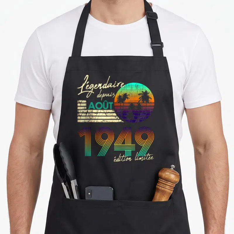Tablier de cuisine noir avec design rétro coloré affichant « Légendaire depuis Août 1949 » sur fond de soleil couchant.
