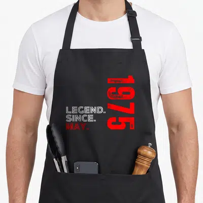 Tablier de cuisine noir avec inscription légende since may 1975 en typographie rouge et blanche.