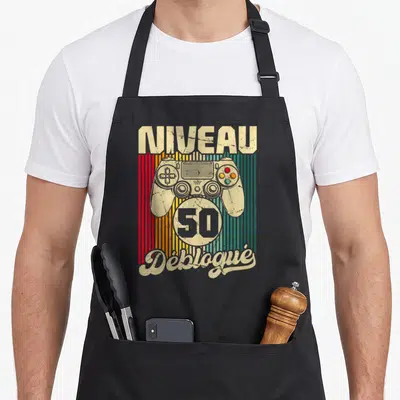 Tablier de cuisine noir avec illustration vintage Niveau 50 Débloqué et manette de jeu vidéo colorée.