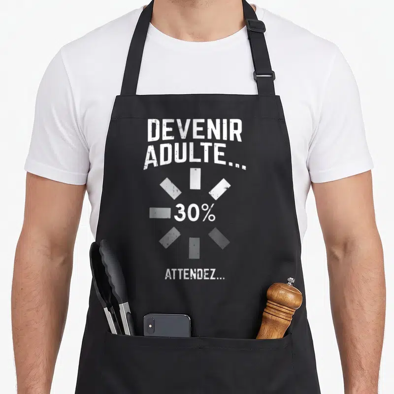 Tablier de cuisine noir avec l'inscription Devenir Adulte 30% Attendez en typographie blanche stylisée.