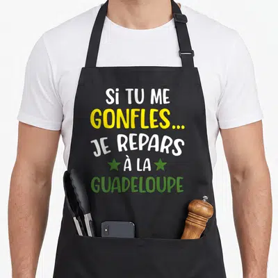Tablier de cuisine noir avec inscription Si tu me gonfles je repars à la Guadeloupe en lettres blanches jaunes et vertes.