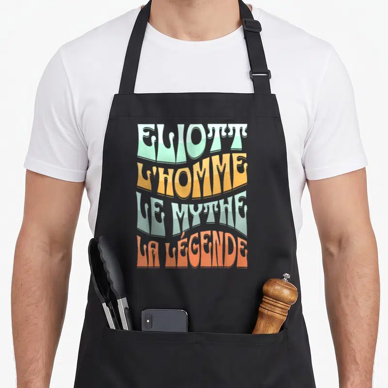 Tablier de cuisine noir avec inscription rétro Eliott L'Homme Le Mythe La Légende en lettres ondulées pastel.