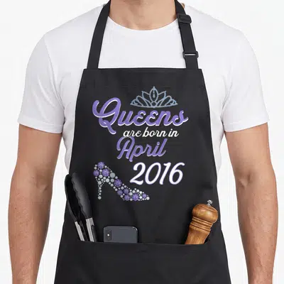 Tablier de cuisine noir avec inscription Queens are born in April 2016, une tiare et un talon de chaussure scintillants en violet.