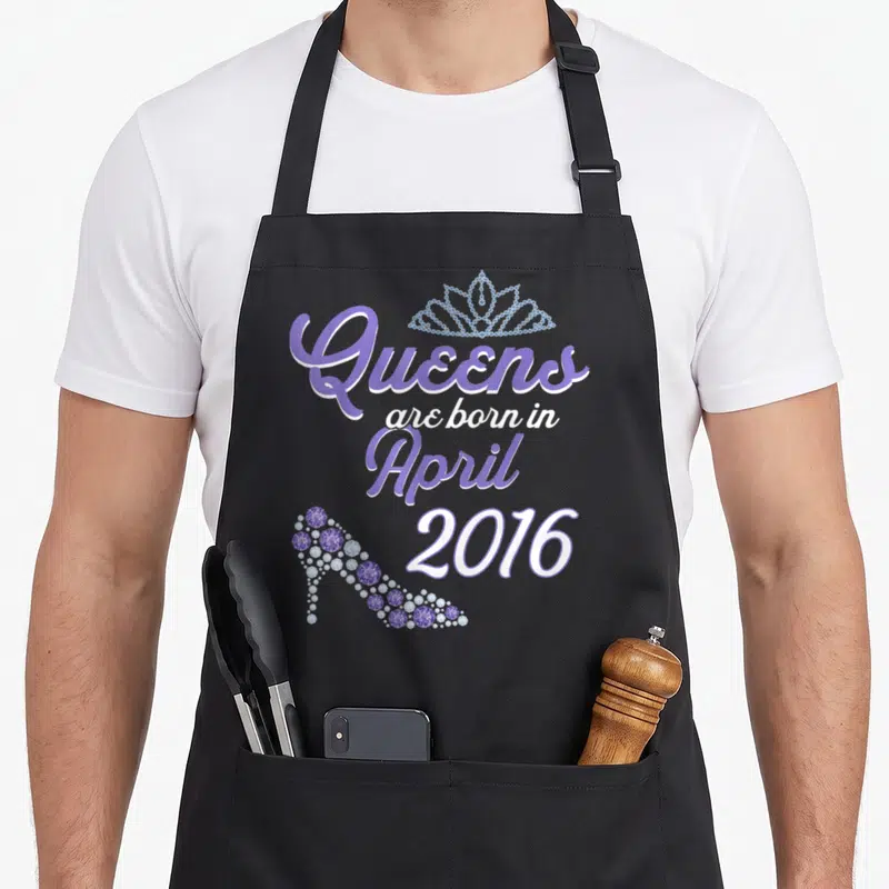 Tablier de cuisine noir avec inscription Queens are born in April 2016, une tiare et un talon de chaussure scintillants en violet.