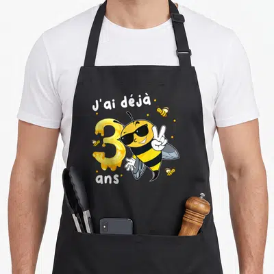 Tablier de cuisine noir avec une abeille aux lunettes noires et un chiffre 3 coulant de miel.