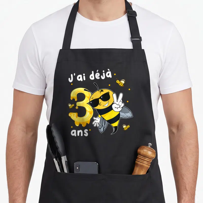 Tablier de cuisine noir avec une abeille aux lunettes noires et un chiffre 3 coulant de miel.