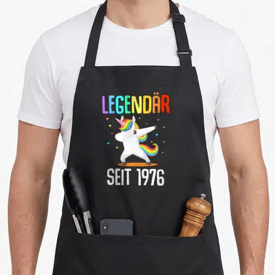 Tablier de cuisine noir avec licorne blanche effectuant un dab et texte multicolore Legendär seit 1976
