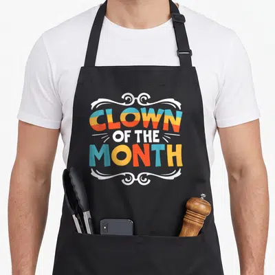Tablier de cuisine noir avec inscription colorée Clown of the Month encadrée de volutes blanches stylisées.