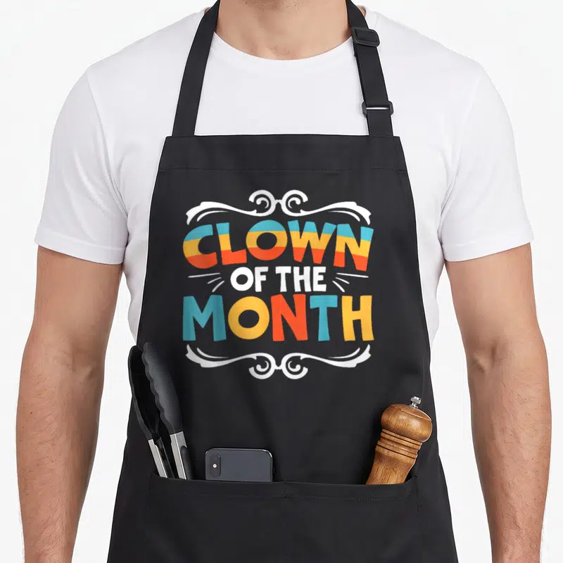 Tablier de cuisine noir avec inscription colorée Clown of the Month encadrée de volutes blanches stylisées.