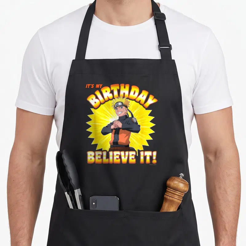 Tablier de cuisine noir avec Naruto Shippuden et le texte It's My anniversaire Believe It en lettres jaunes et oranges.