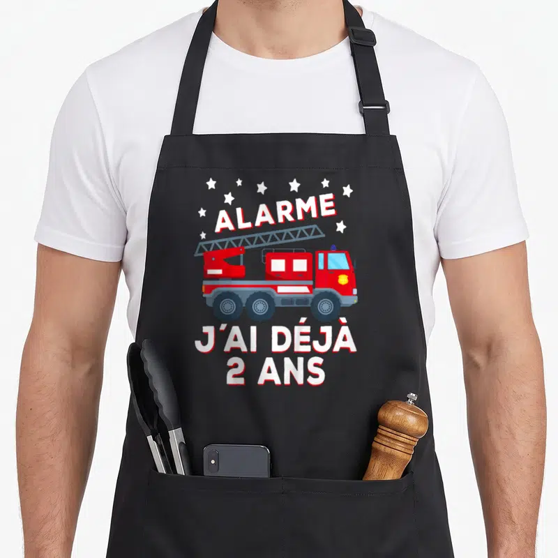 Tablier de cuisine noir avec illustration de camion de pompiers rouge et texte blanc Alarme j'ai déjà 2 ans entouré d'étoiles.
