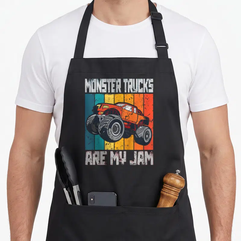Tablier de cuisine noir avec illustration monster truck orange et texte blanc vintage sur bandes colorées.