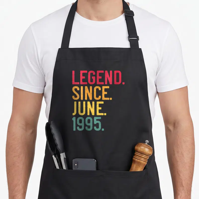 Tablier de cuisine noir avec inscription colorée Legend Since June 1995 en typographie vintage dégradée.