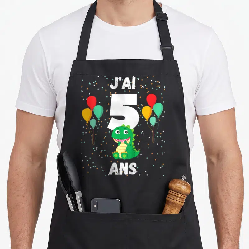 Tablier de cuisine noir avec un dinosaure vert, le chiffre 5 et des ballons colorés.