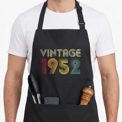 Tablier de cuisine noir avec l'inscription Vintage 1952 en lettres rayées multicolores sur fond uni.