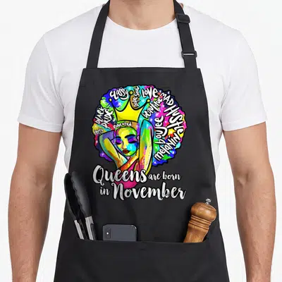 Tablier de cuisine noir avec une illustration colorée d'une femme coiffée d'un diadème jaune et de texte blanc soulignant la fierté noire.