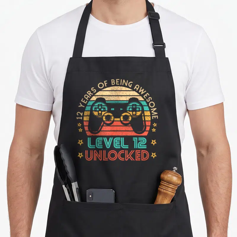 Tablier de cuisine noir avec illustration vintage manette de jeu et texte Level 12 Unlocked.