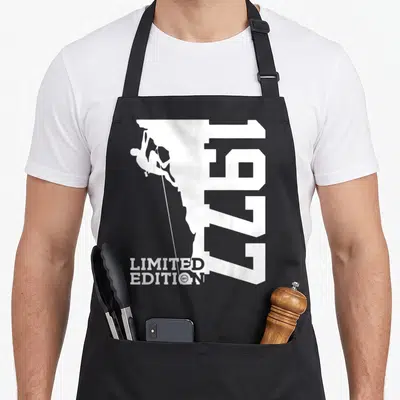 Tablier de cuisine noir avec silhouette d'alpiniste, chiffres 1977 et texte Limited Edition No1 en blanc.