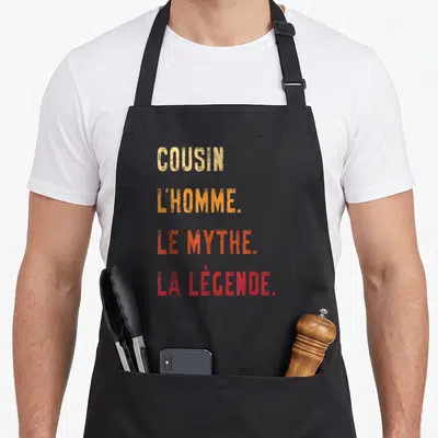 Tablier de cuisine noir avec inscription colorée Cousin l'homme le mythe la légende en typographie dégradée.