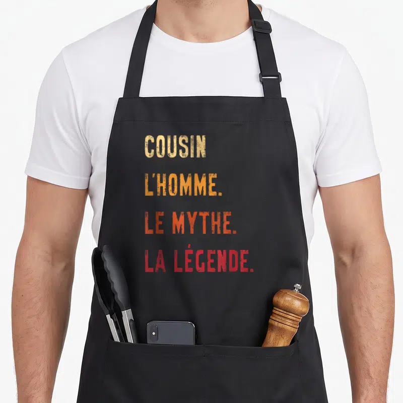 Tablier de cuisine noir avec inscription colorée Cousin l'homme le mythe la légende en typographie dégradée.