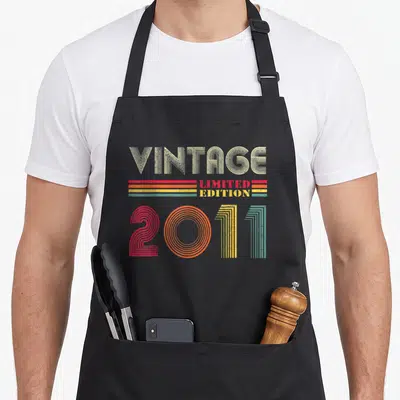 Tablier de cuisine noir avec inscription Vintage 2011 Limited Edition en lettres rétro multicolores.