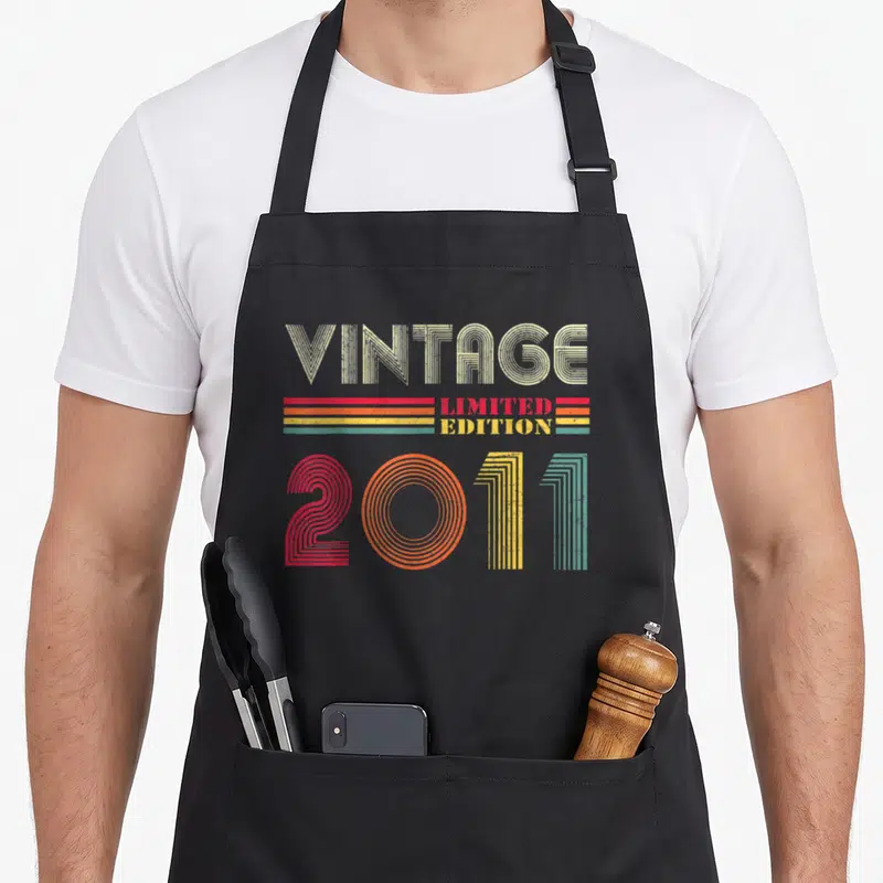 Tablier de cuisine noir avec inscription Vintage 2011 Limited Edition en lettres rétro multicolores.