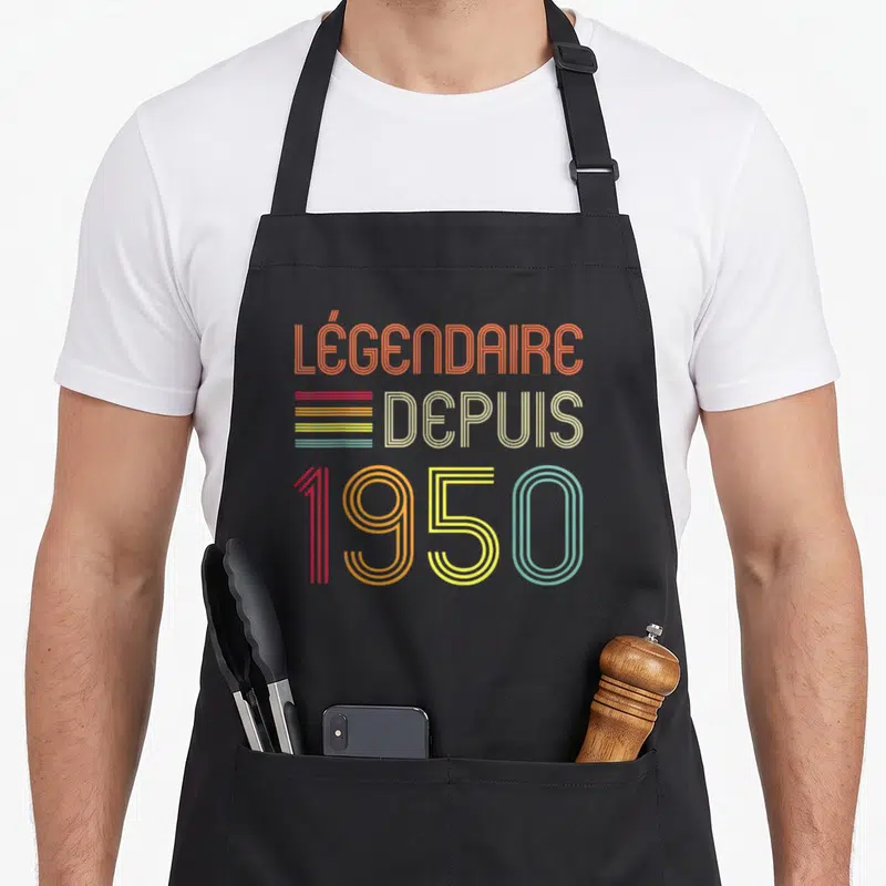 Tablier de cuisine noir avec inscription Légendaire Depuis 1950 en typographie rétro multicolore.