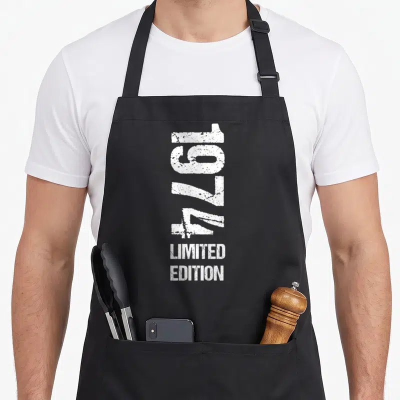 Tablier de cuisine noir avec l'année 1974 et les mots Limited Edition imprimés en blanc vertical.