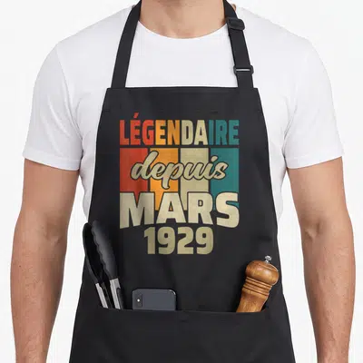 Tablier de cuisine noir avec inscription colorée Légendaire depuis Mars 1929 sur fond de bandes verticales rétro.