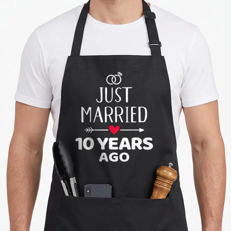 Tablier de cuisine noir avec inscription Just Married 10 Years Ago, cœurs et anneaux nuptiaux blancs.
