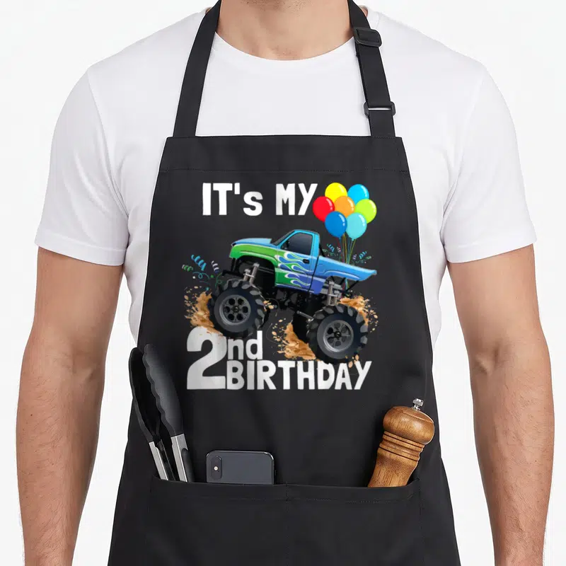 Tablier de cuisine noir avec un Monster Truck bleu, des ballons et le texte It's My 2nd anniversaire en blanc.