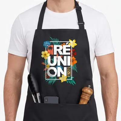Tablier de cuisine noir avec inscription Réunion 974 entourée de fleurs tropicales jaunes, rouges et bleues ainsi que de feuilles vertes.
