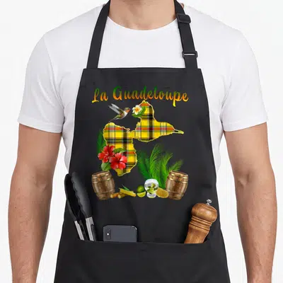 Tablier de cuisine noir avec carte de Guadeloupe en madras, colibri, fleurs d'hibiscus et barils de rhum.