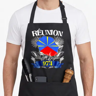 Tablier de cuisine noir avec le drapeau de La Réunion, le numéro 974 et deux geckos blancs encadrant des fleurs tropicales.