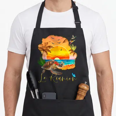 Tablier de cuisine noir avec illustration d'une tortue, d'un soleil et du texte La Réunion en lettres dorées.