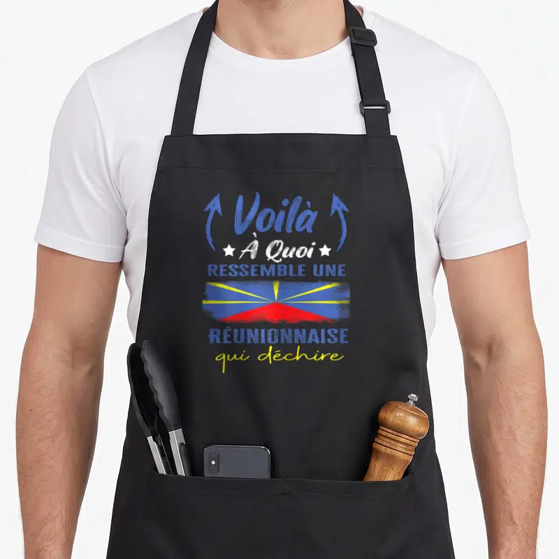 Tablier de cuisine noir avec le texte Voilà à quoi ressemble une Réunionnaise qui déchire au-dessus d'un motif graphique aux couleurs du drapeau.
