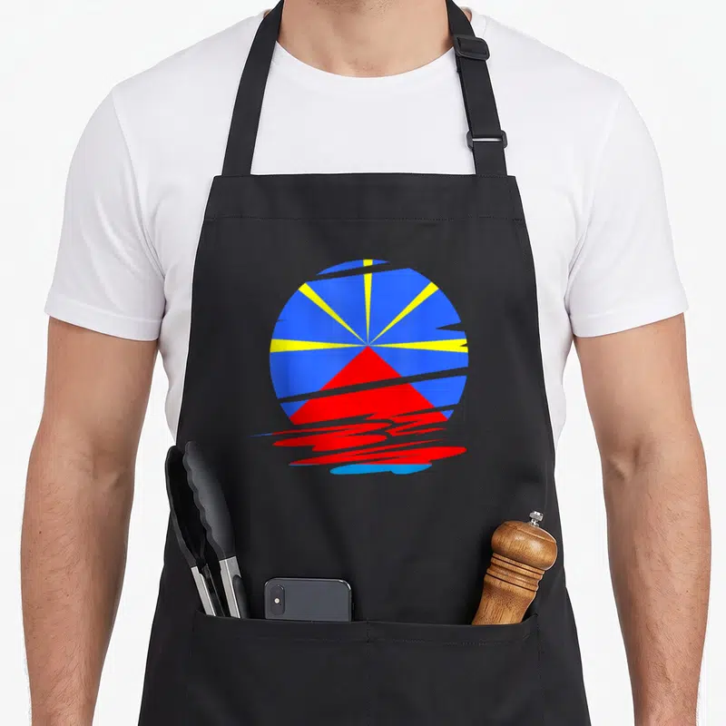 Tablier de cuisine noir avec motif circulaire bleu jaune et rouge évoquant le soleil et le volcan de l'île de la Réunion.