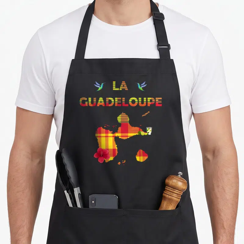Tablier de cuisine noir avec une carte de la Guadeloupe en tissu madras, des colibris et un hibiscus rouge imprimé sur le devant.