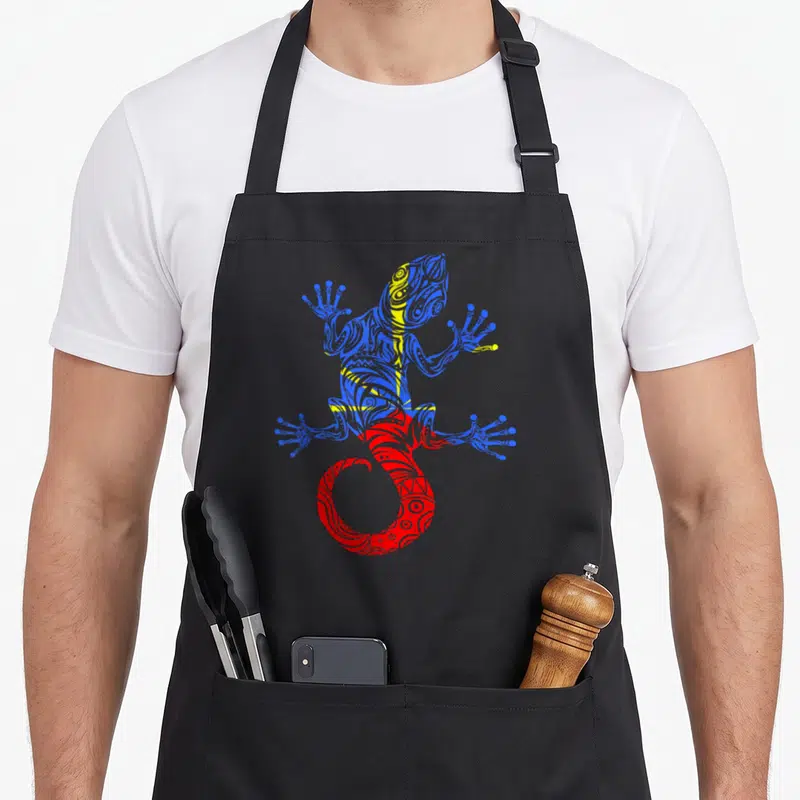 Tablier de cuisine noir avec un gécko stylisé aux motifs tribaux bleus jaunes et rouges représentant l'île de la Réunion.