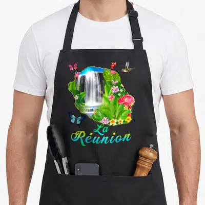 Tablier de cuisine noir avec illustration colorée de l'île de La Réunion, cascade, fleurs tropicales, papillons et colibri.