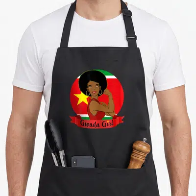 Tablier de cuisine noir avec illustration Gwada Girl et drapeau guadeloupéen en arrière-plan circulaire rouge vert et blanc.